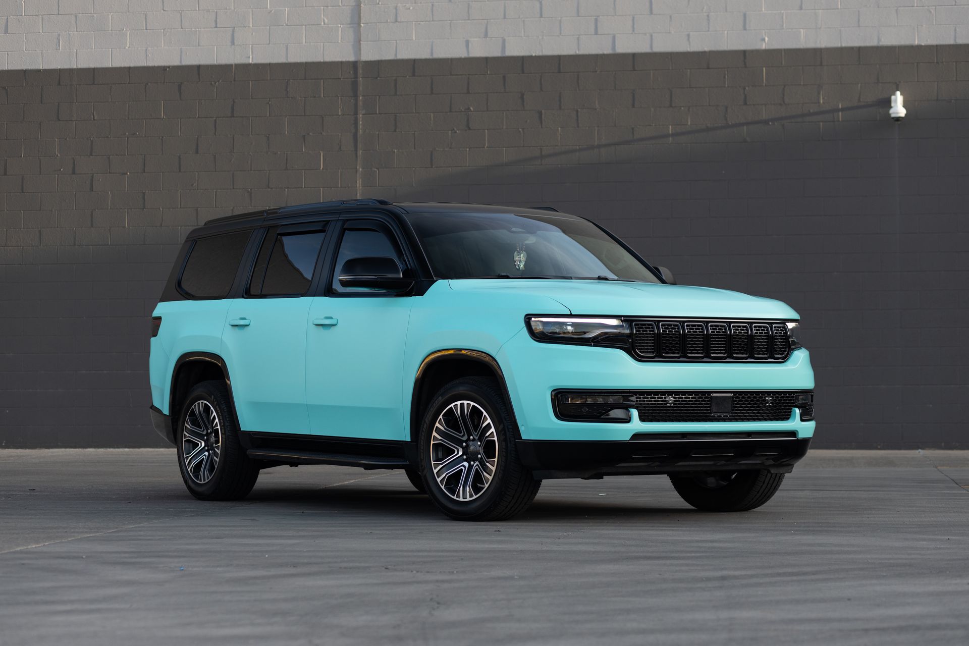 Light blue SUV with a black roof and black wheels parked against a gray wall.