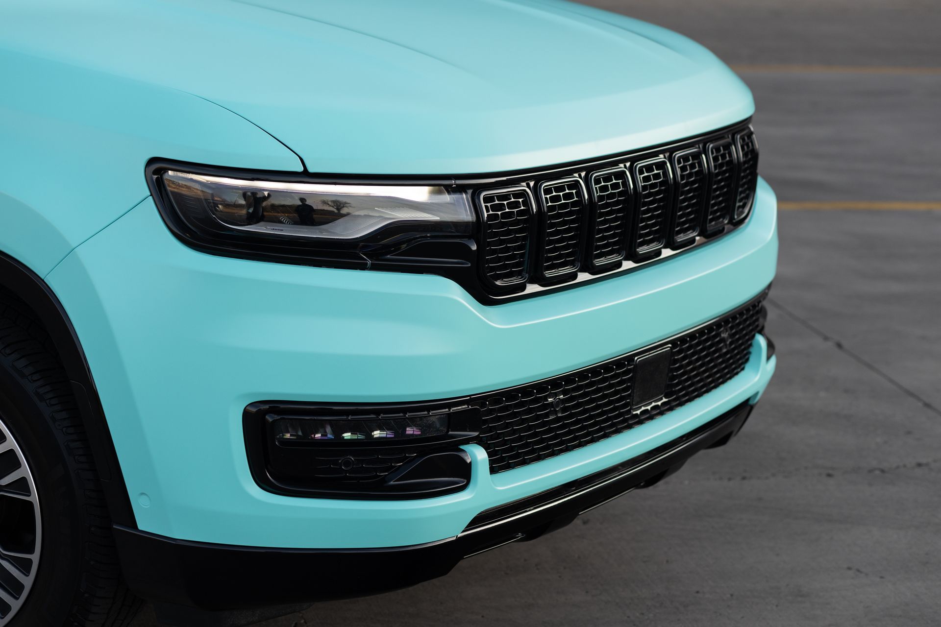 Close-up of a teal SUV's front, with black grill, headlights, and bumper.