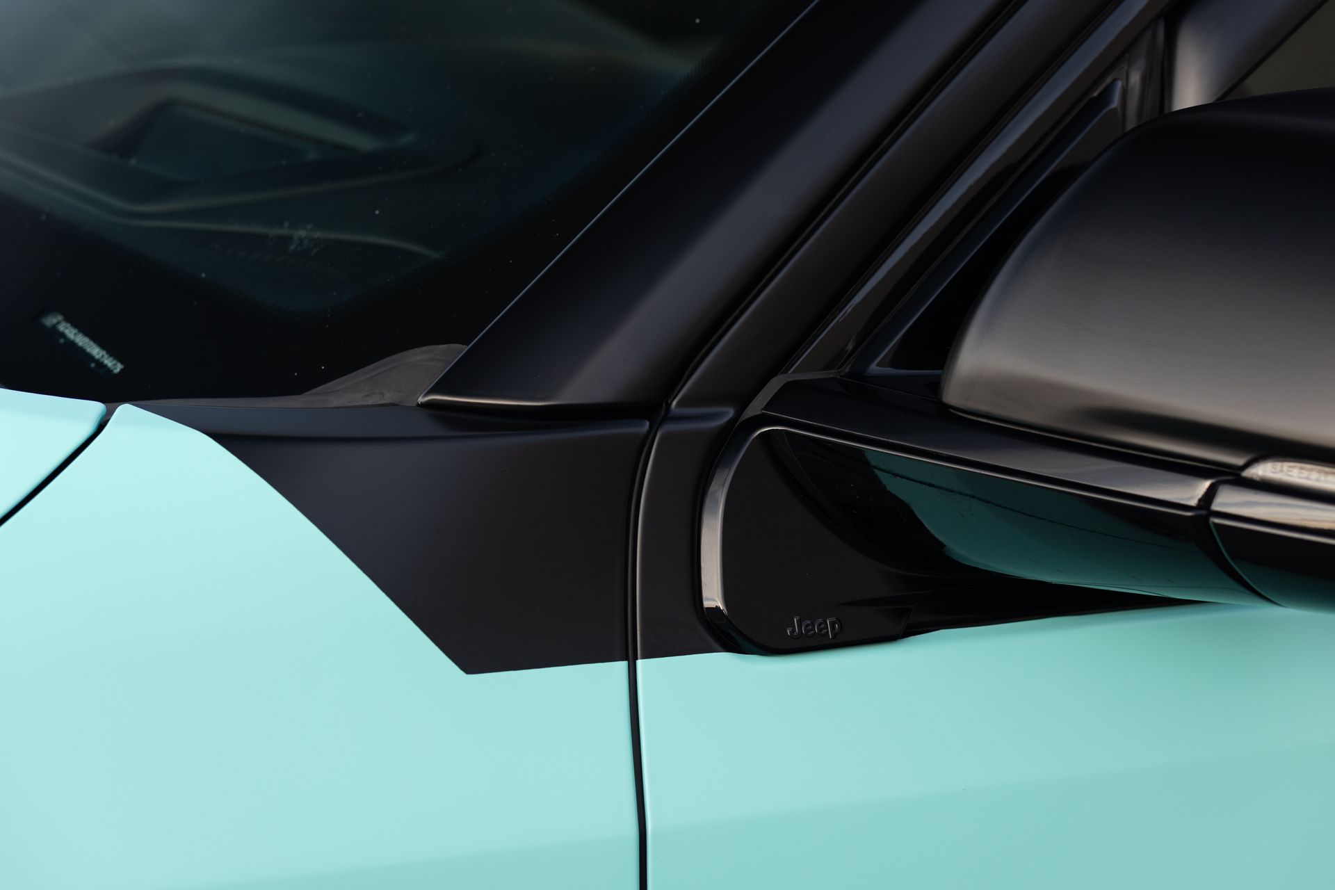 Close-up of a teal car's black trim, including the side mirror and roofline.