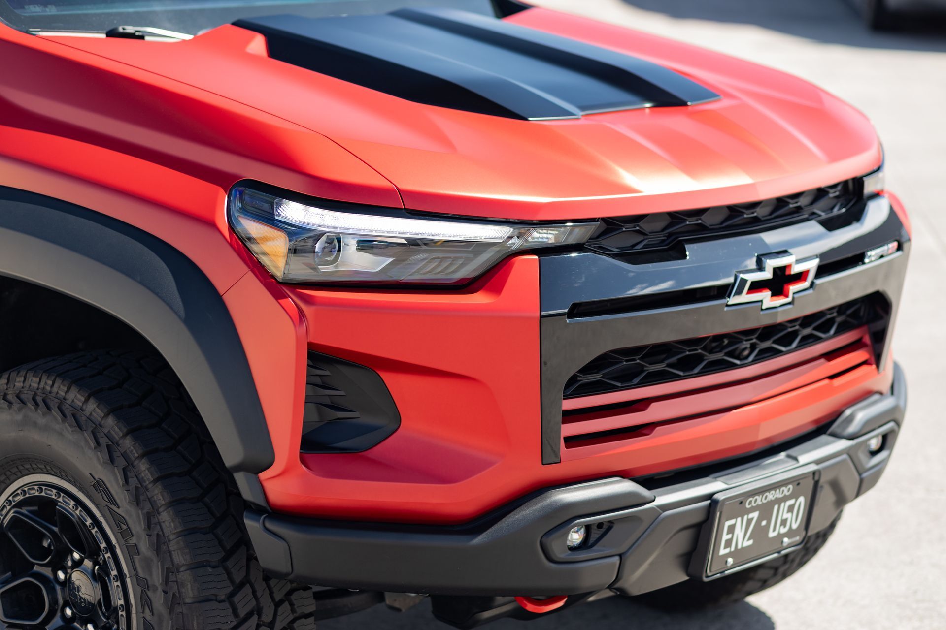 Red Chevrolet truck front end, black hood and grill, gray wheel.