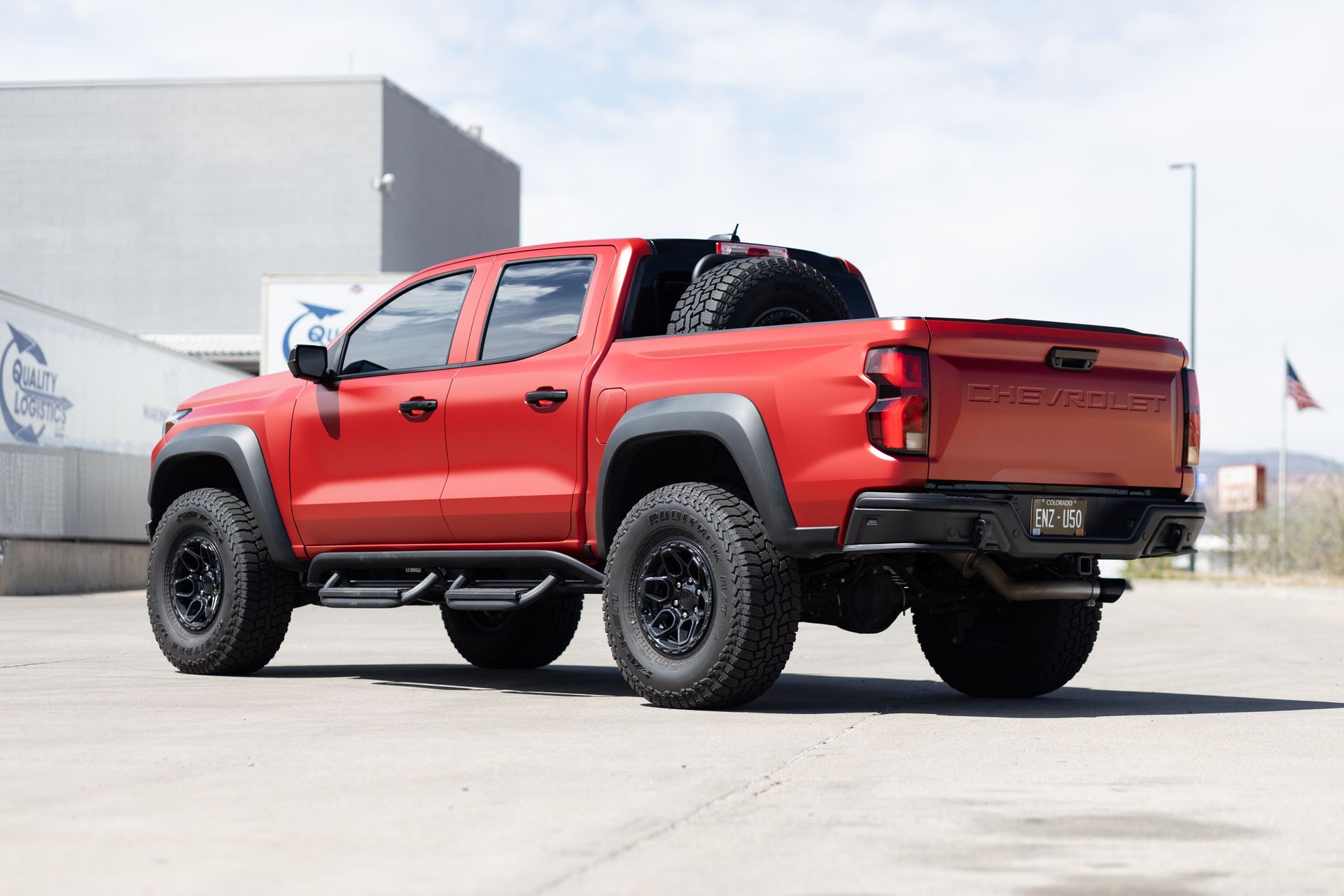 Red lifted pickup truck with black wheels and spare tire on a sunny day.