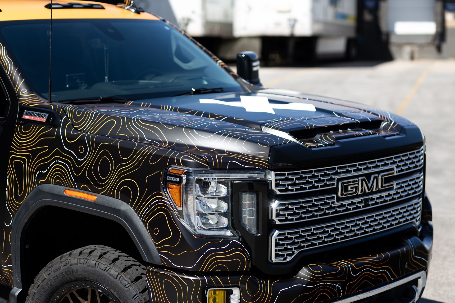 Black and gold GMC truck with topographic design on hood and Texas flag on windshield, parked.