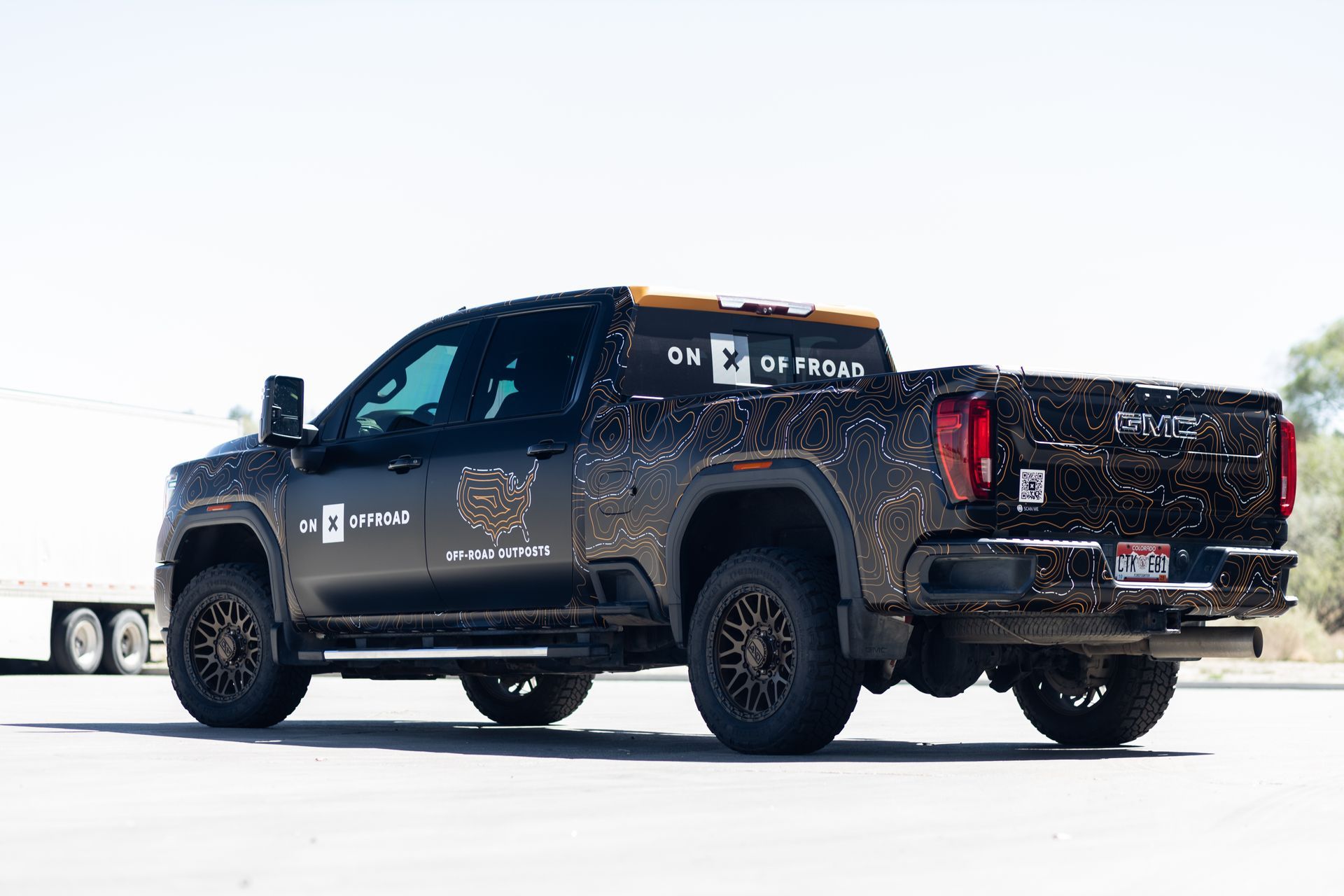 Black GMC truck with bronze wheels and camouflage wrap, parked outdoors.