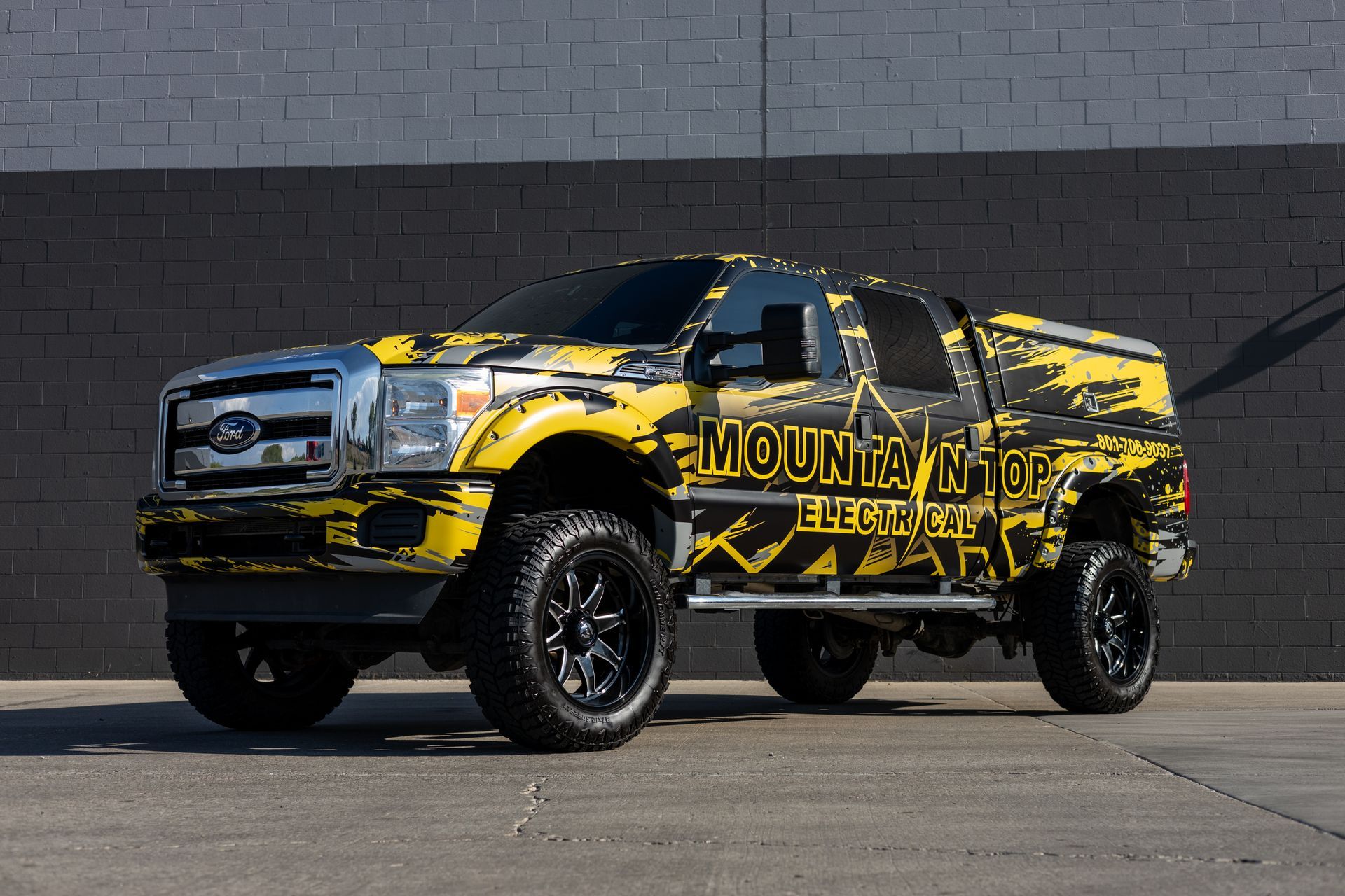 Yellow and black Mountain Electric truck parked against a dark gray wall.