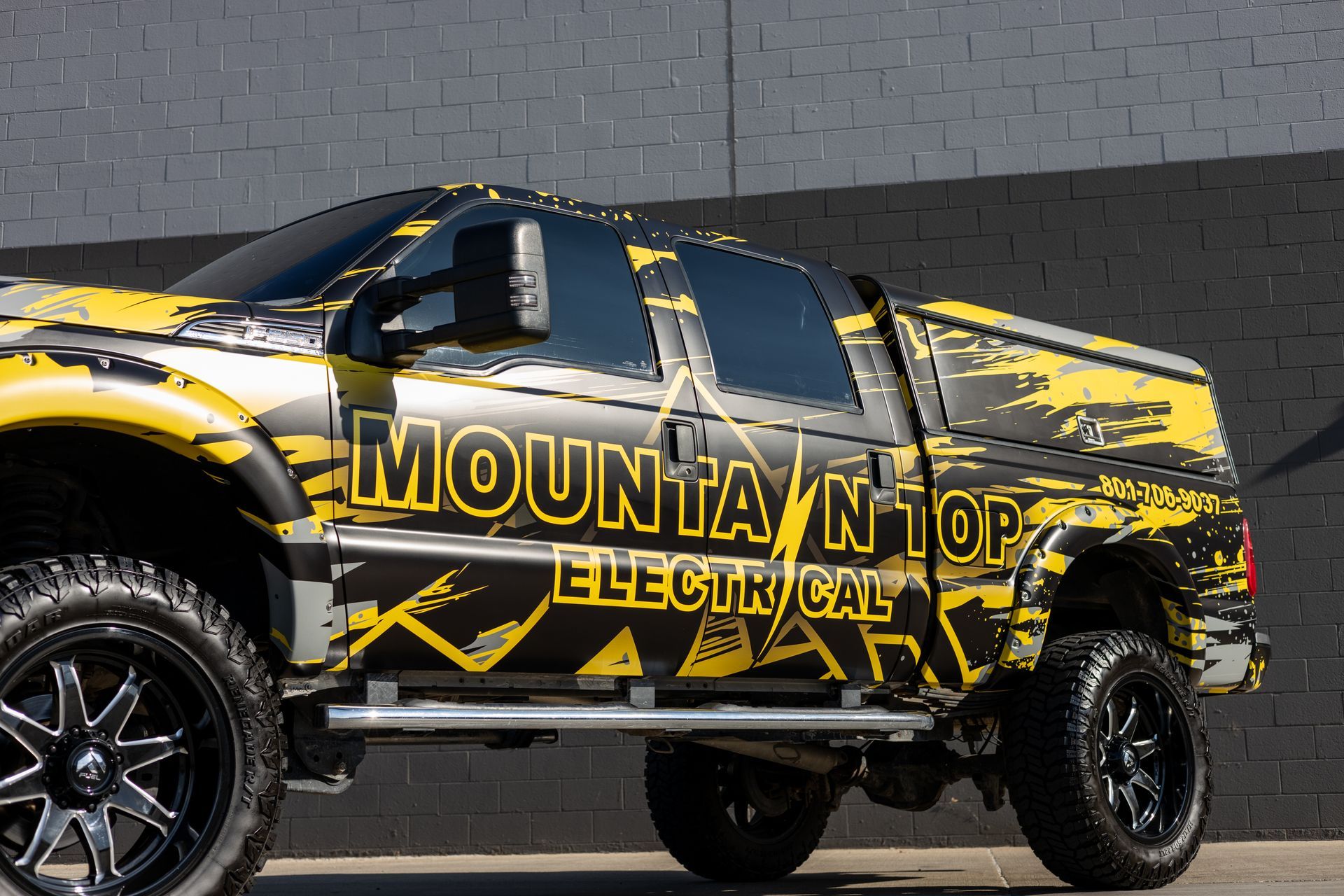 Yellow and black Mountain Top Electrical truck parked in front of a gray building.