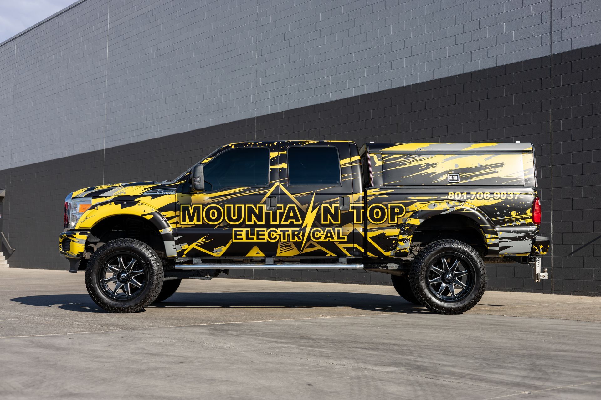 Yellow and black Mountain Top Electrical truck parked in front of a gray wall.