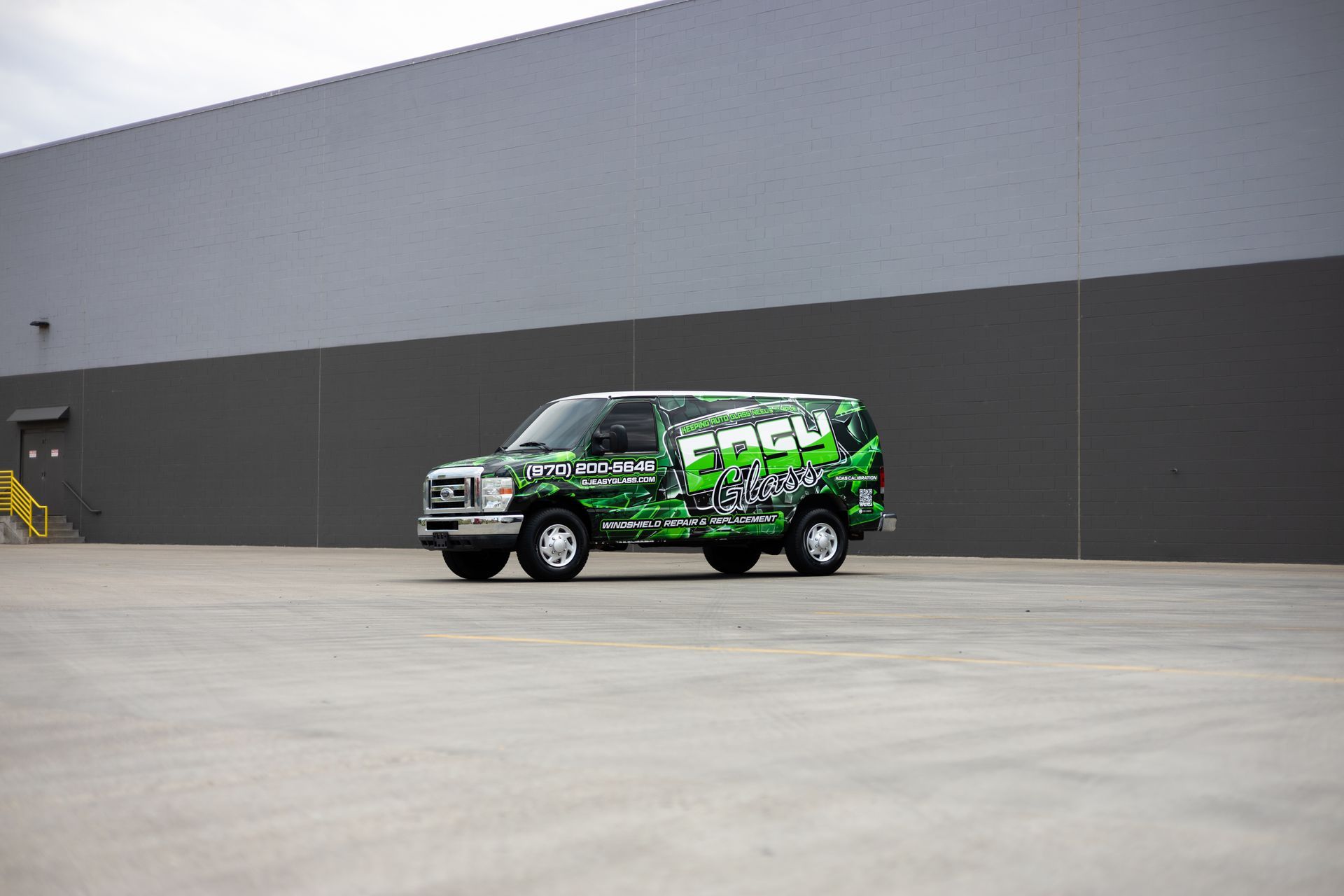 Green and black wrapped van in front of a gray building.