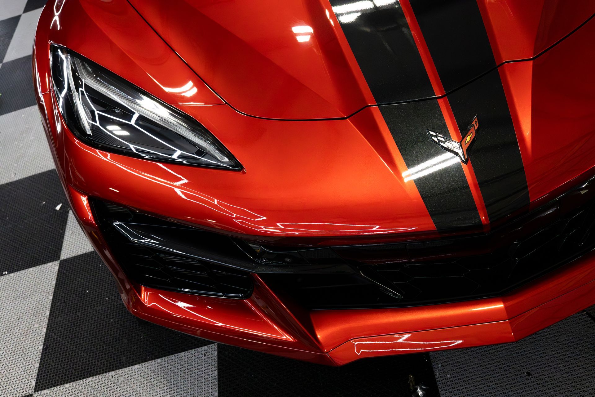 Orange sports car with black racing stripes on a checkered floor.
