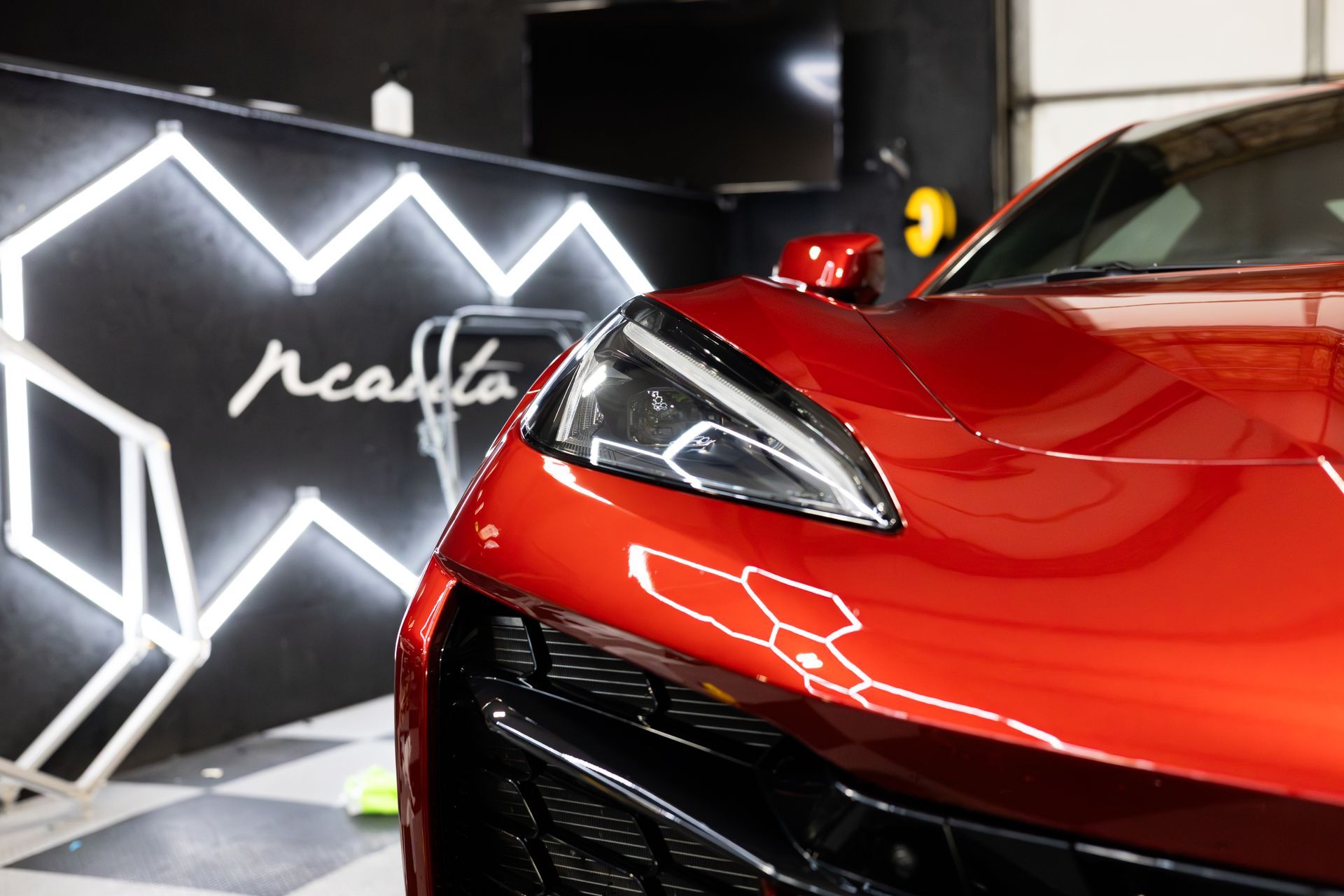 Red sports car front end; black grill, shiny paint; illuminated sign in background.
