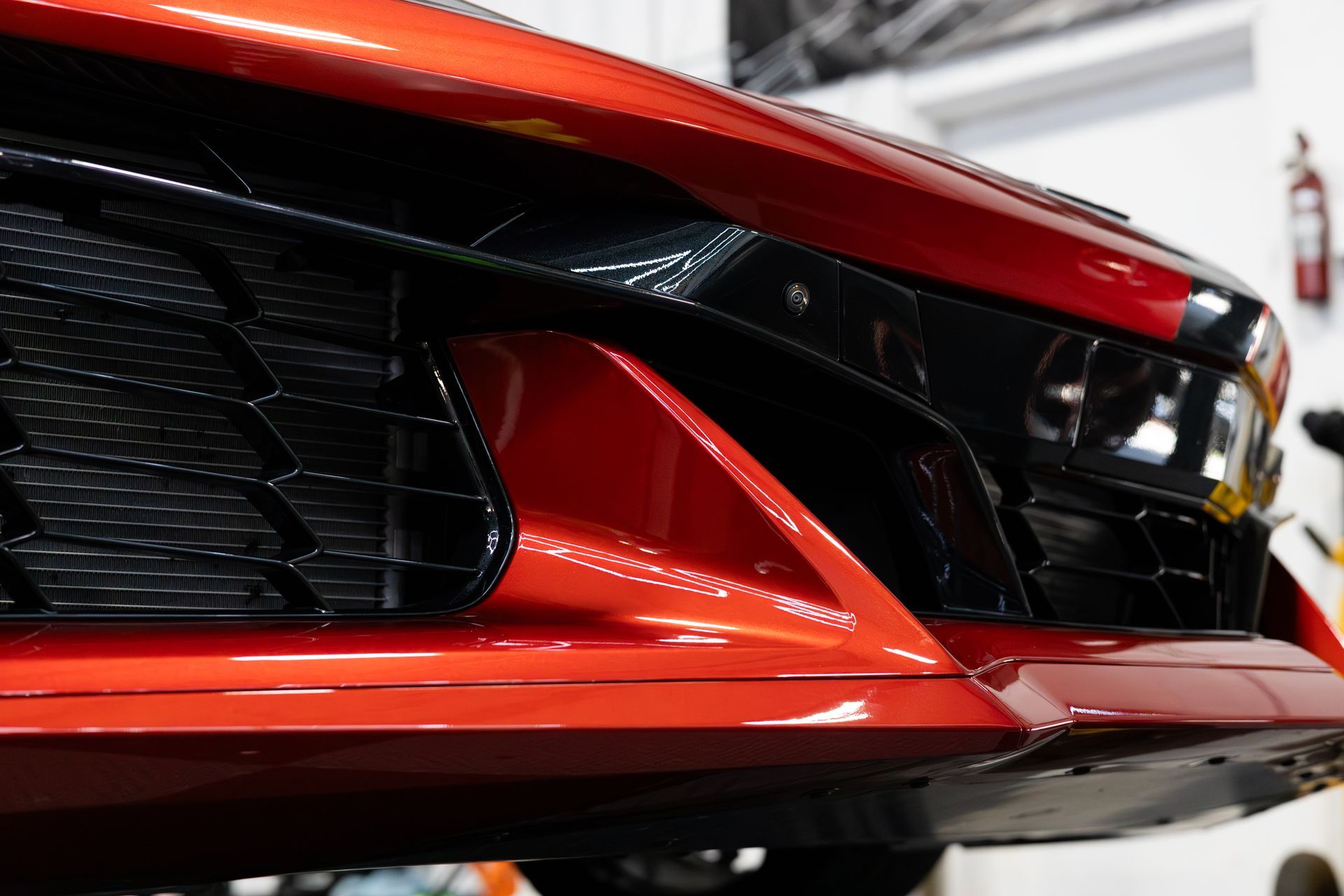 Red sports car's front bumper, black grille, and side vents, indoors.