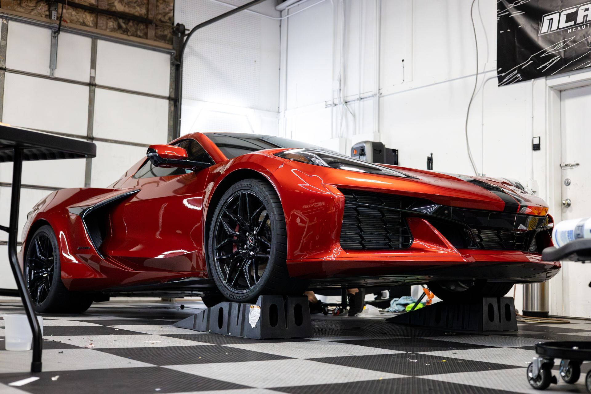 Red sports car on blocks inside a garage with black and white checkered floor.