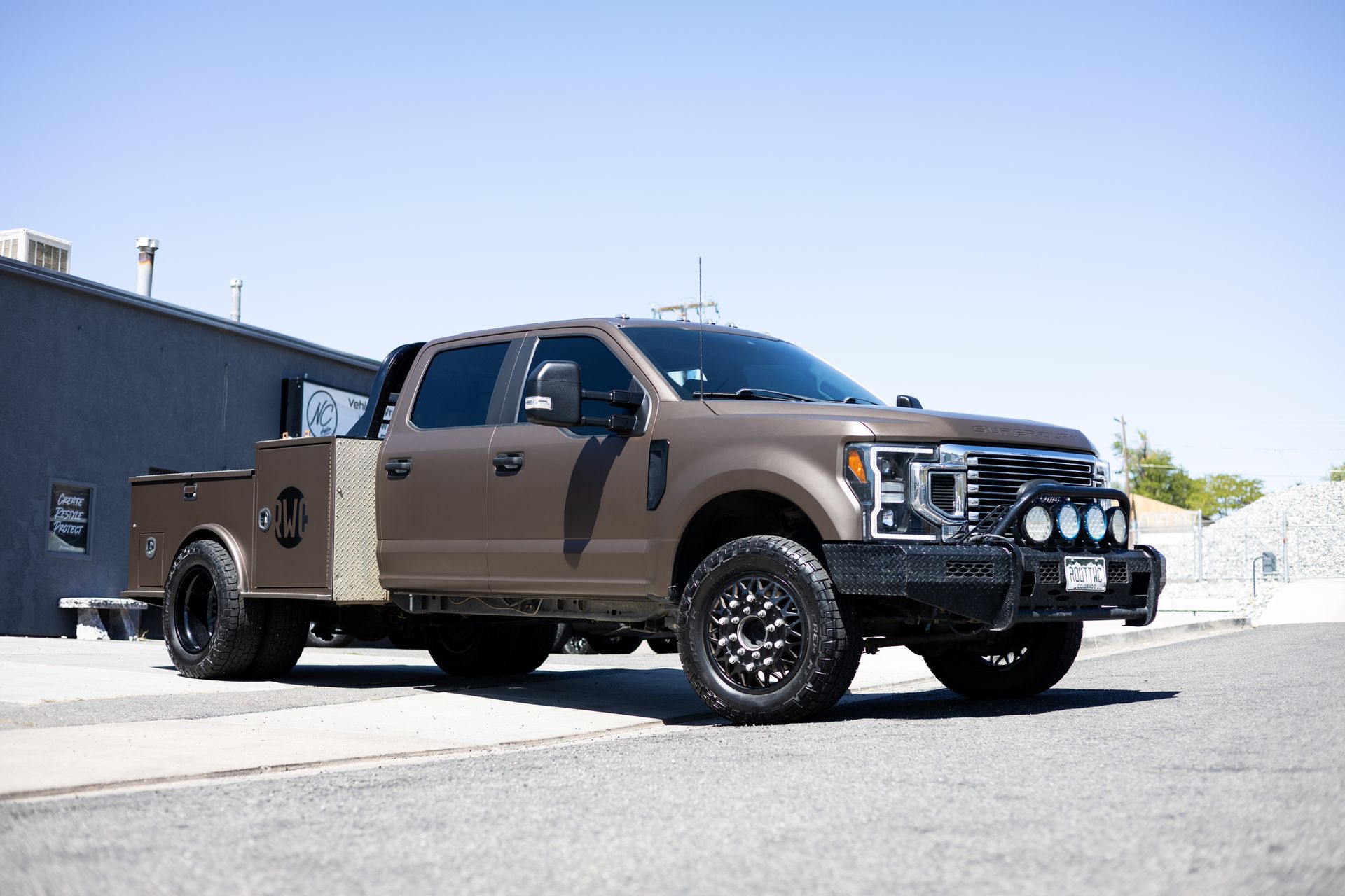 Brown, heavy-duty pickup truck parked on asphalt in front of a building on a sunny day.