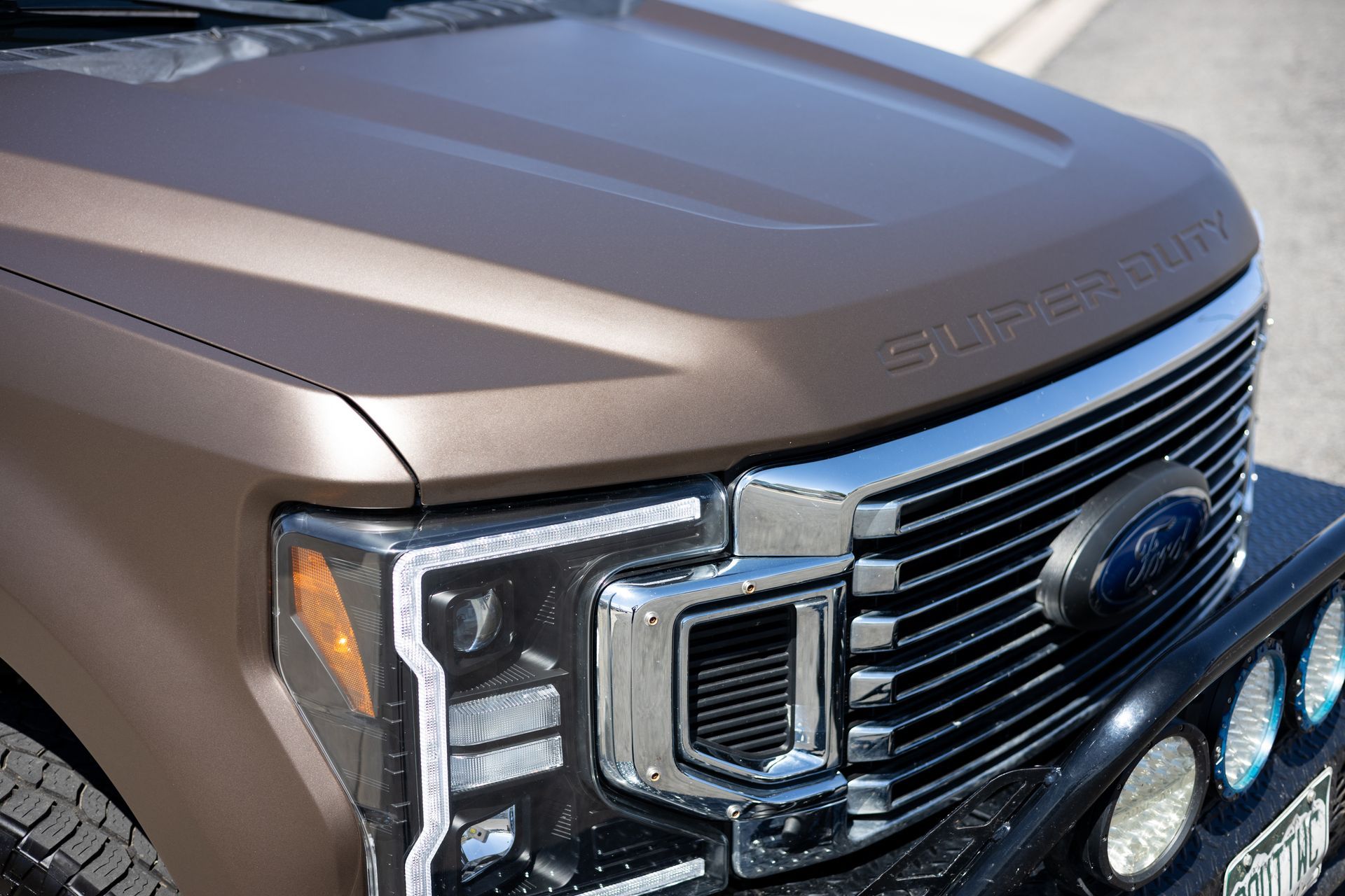 Brown Ford Super Duty truck's front end with chrome grille, headlights, and 