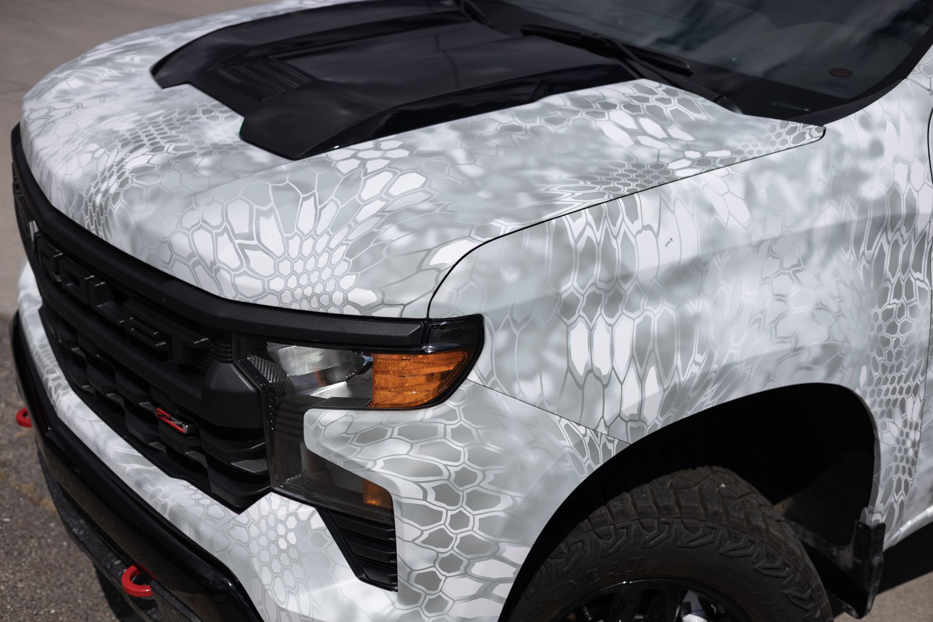 White camouflage-wrapped Chevy Silverado truck. Black hood. Black grille. Gray and white camouflage.