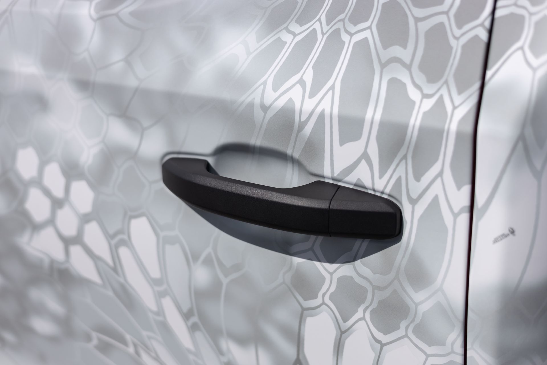 Black car door handle against a white and gray geometric patterned background.