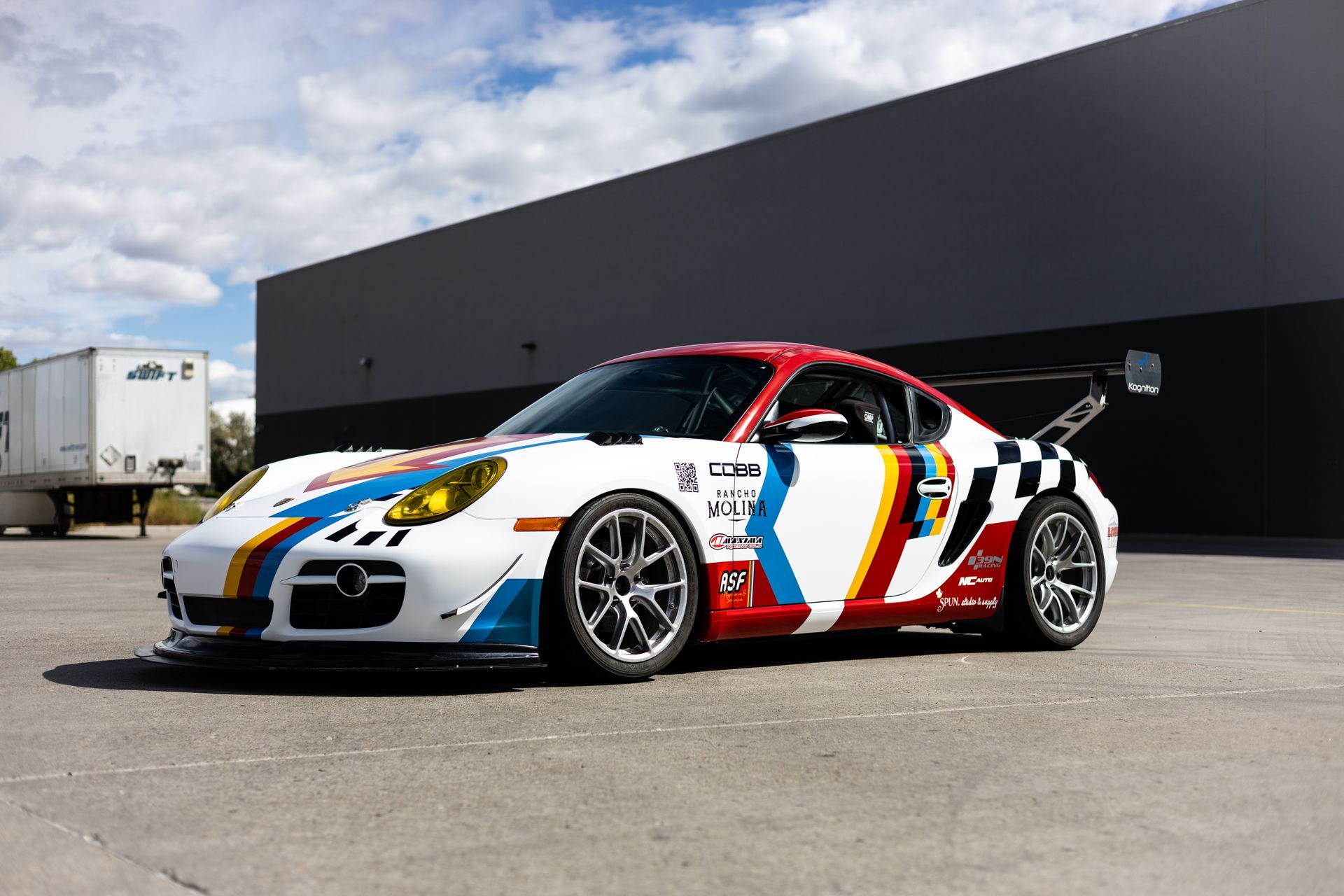 White and red race car with blue and yellow accents, parked in front of a building.
