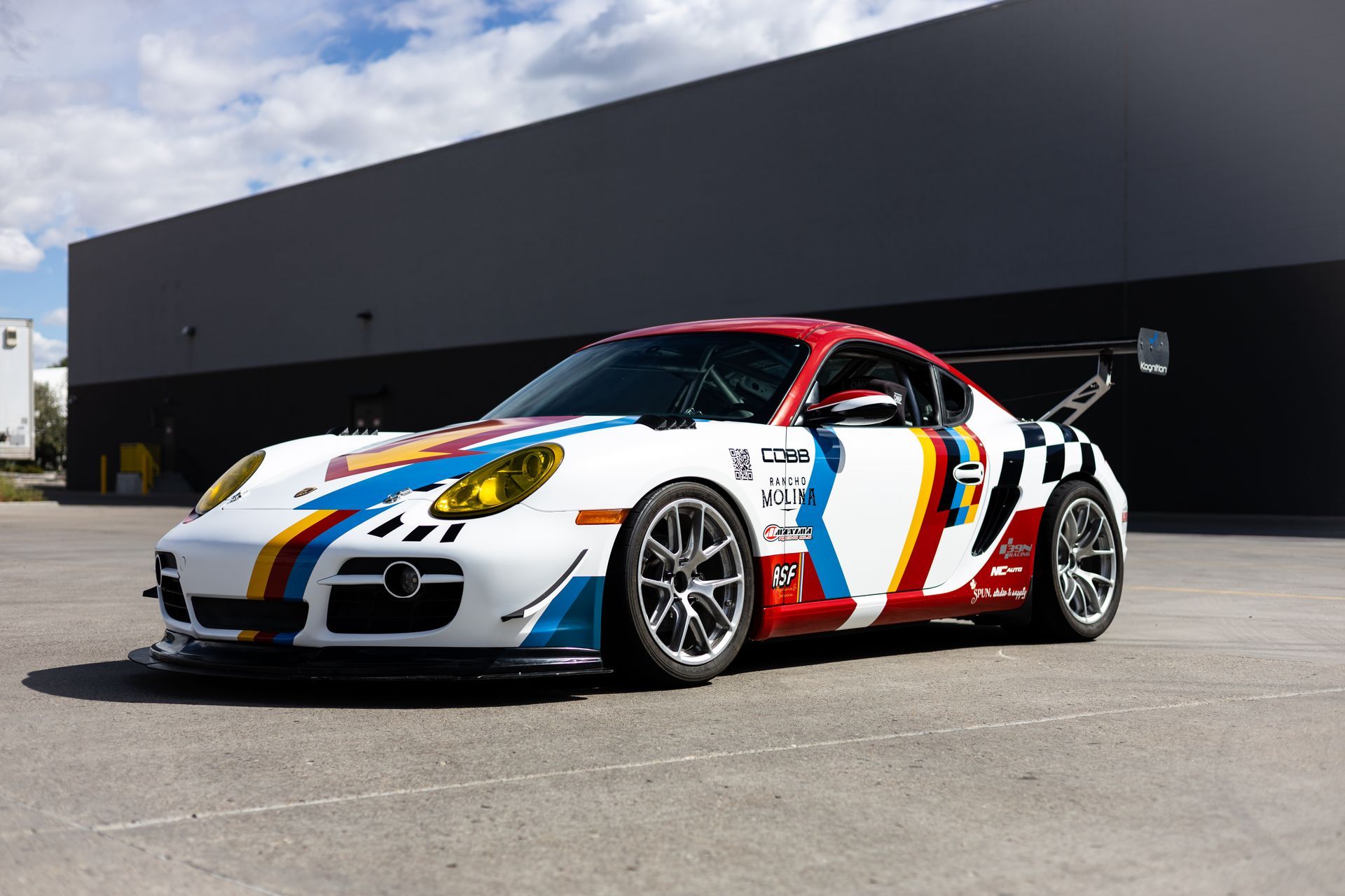 White and colorful race car with a large rear wing parked outside a building.