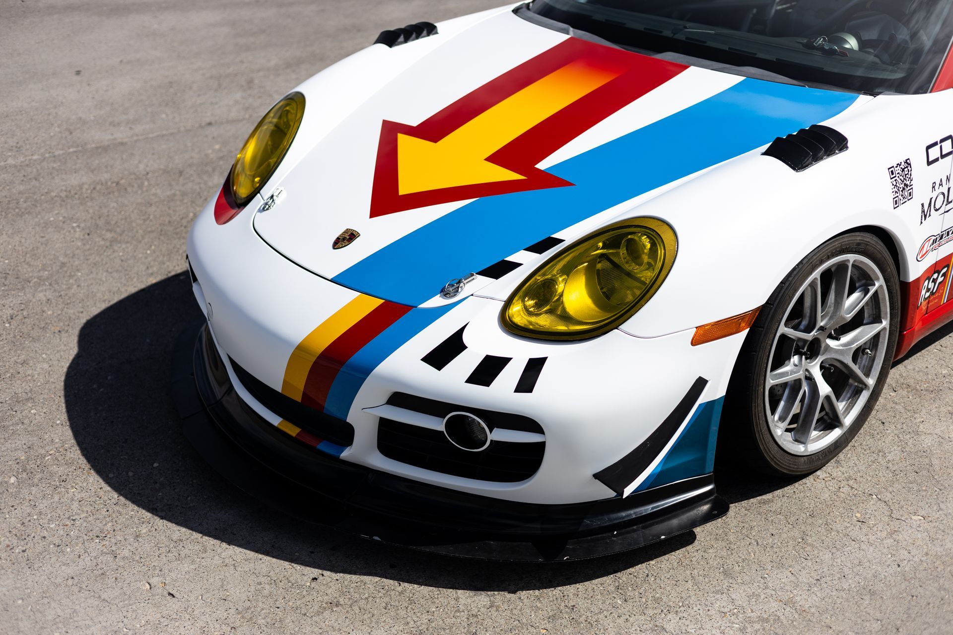 White Porsche race car with colorful arrow design and yellow headlights.