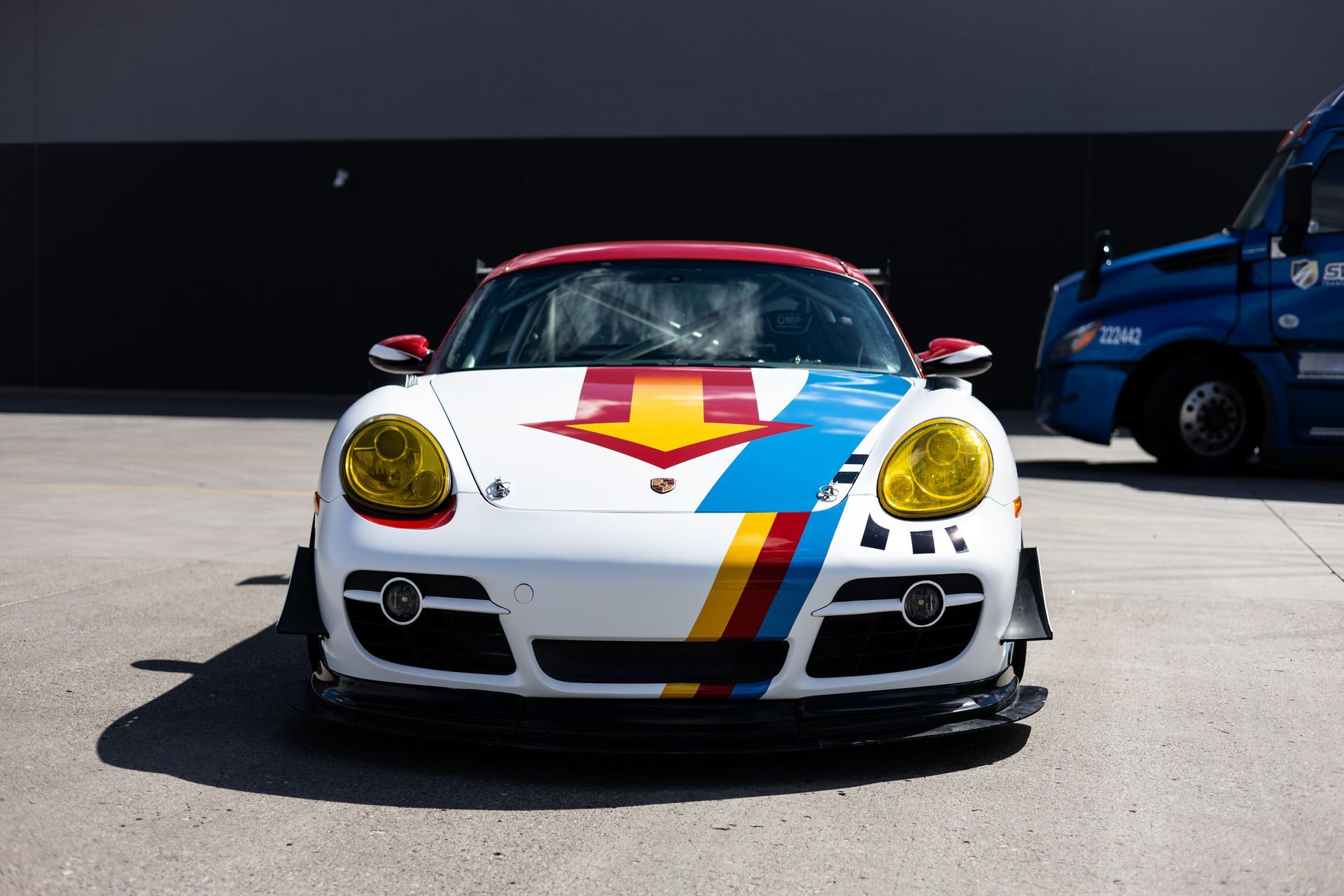 White Porsche sports car with colorful racing stripes and yellow headlights, parked outdoors.