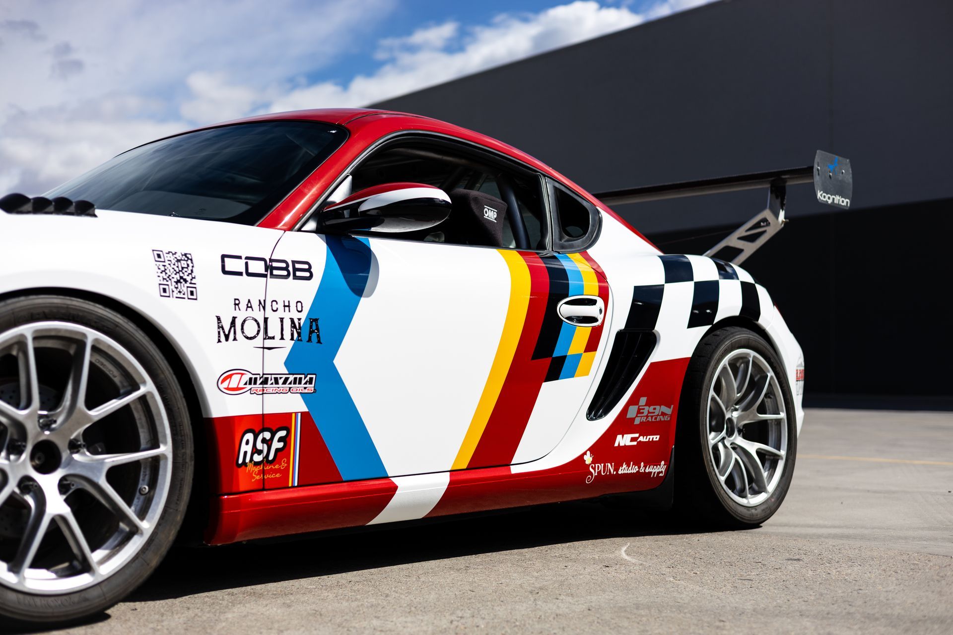 Race car, white with red and blue accents, black and white checkered flag, wing, sunny outdoor setting.