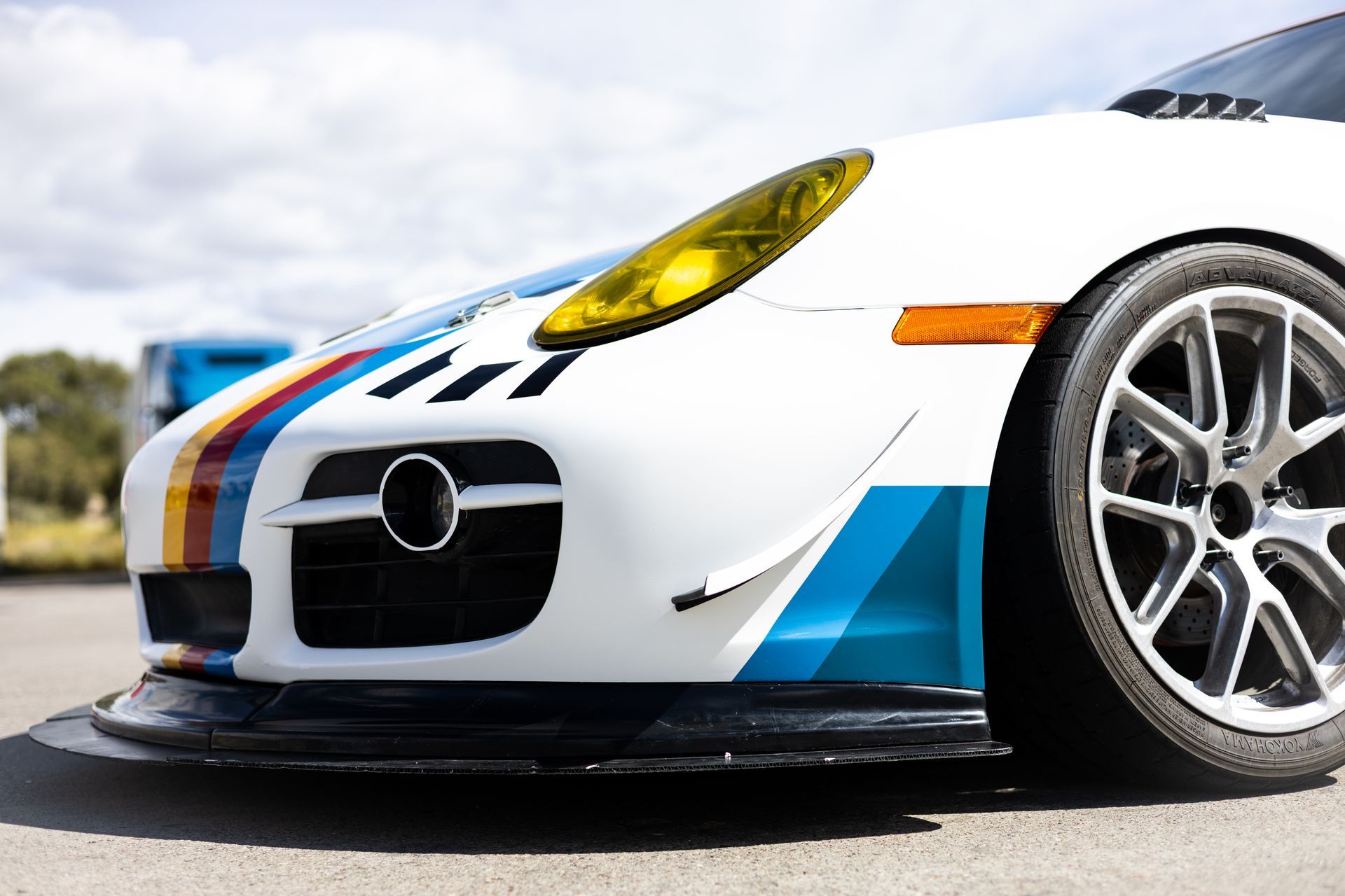 White Porsche sports car with blue and rainbow stripes, yellow headlight.