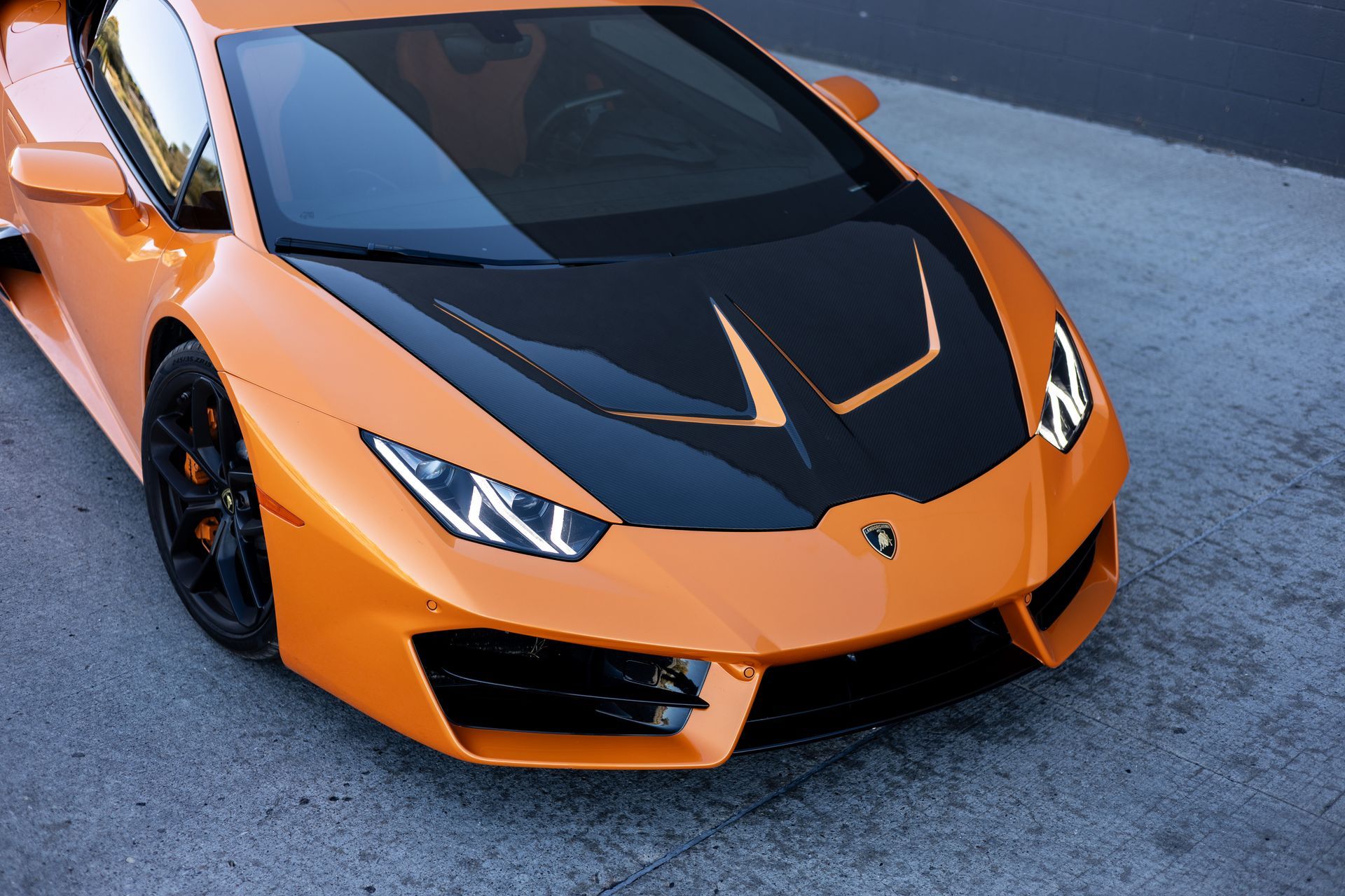 Orange Lamborghini sports car with black hood details, parked on pavement.