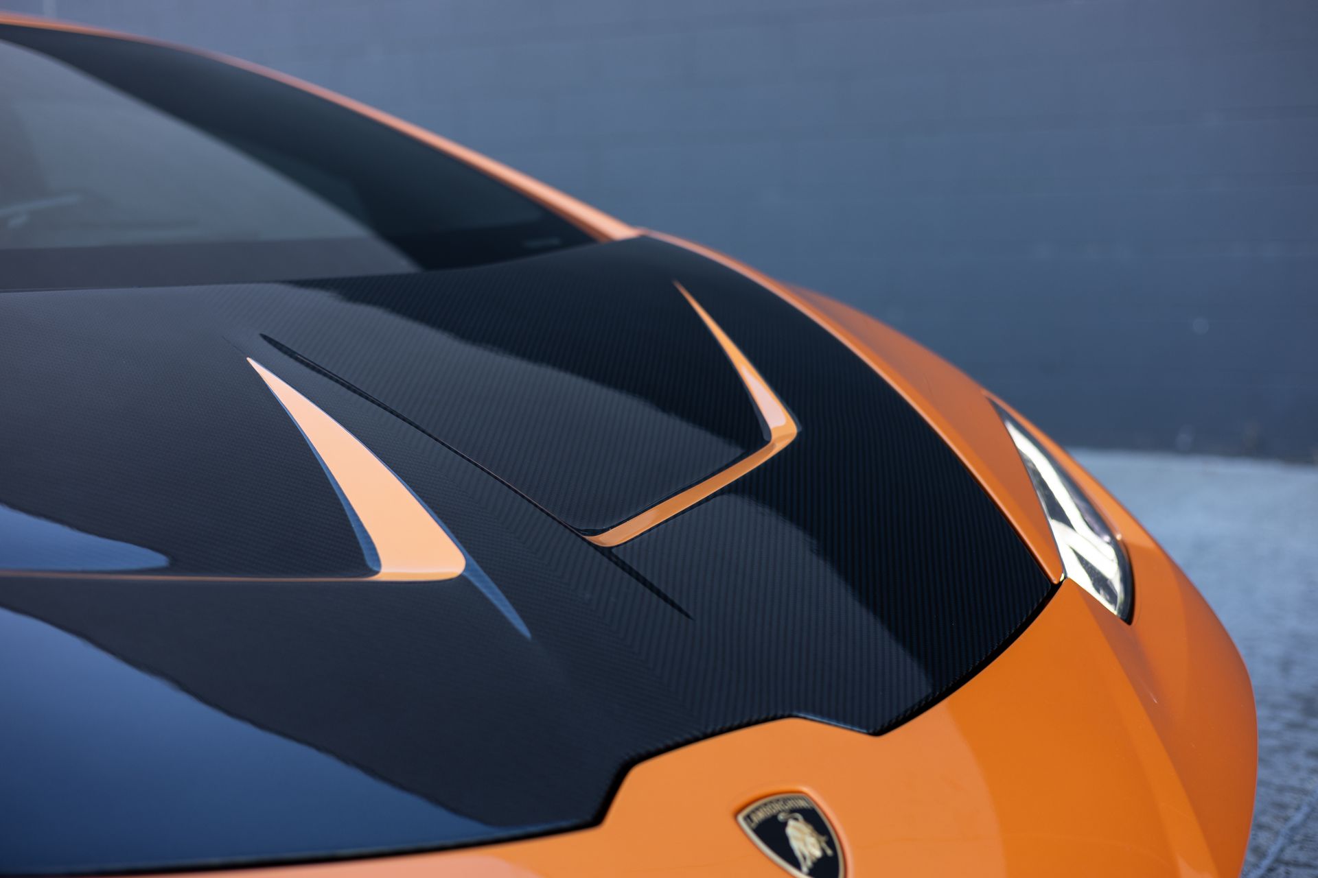 Orange Lamborghini car hood with black carbon fiber detailing.