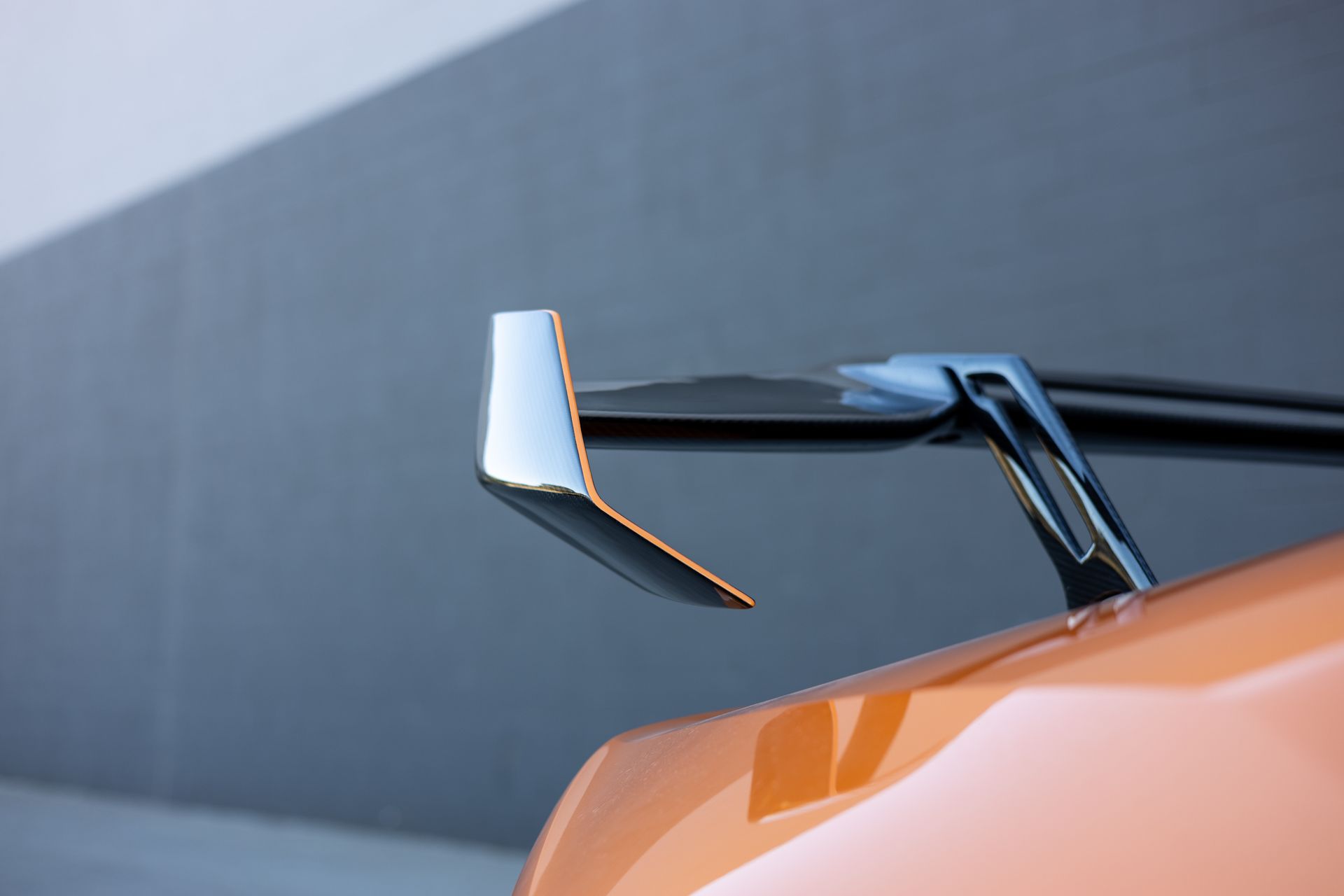 Orange car wing with chrome trim angled upward against a neutral gray wall.