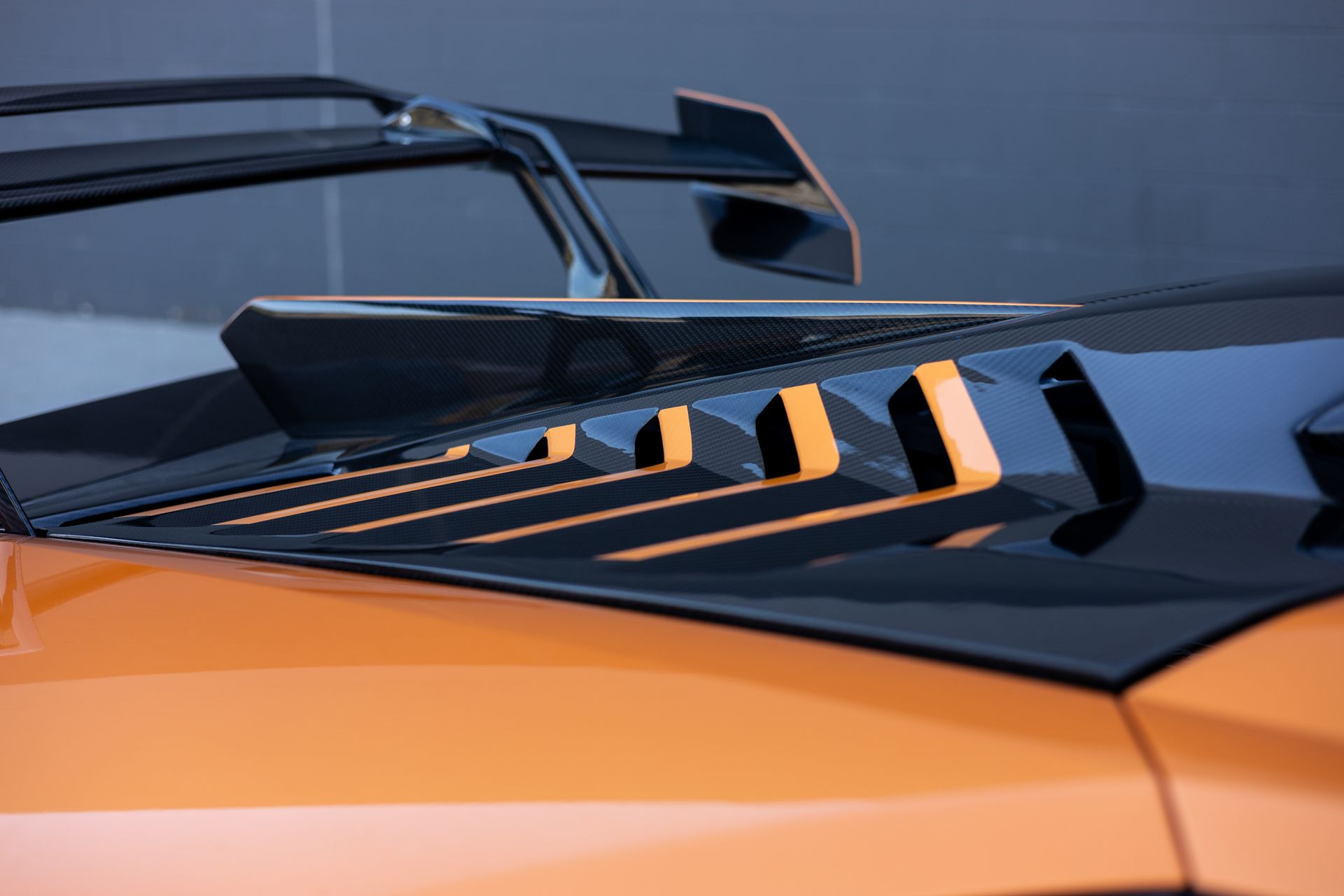 Orange car hood with black vents and spoiler; close-up.