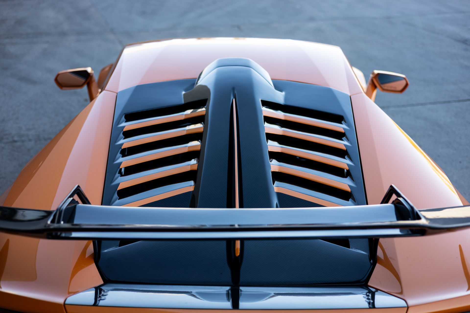 Orange sports car, rear view, showing engine vents and spoiler.