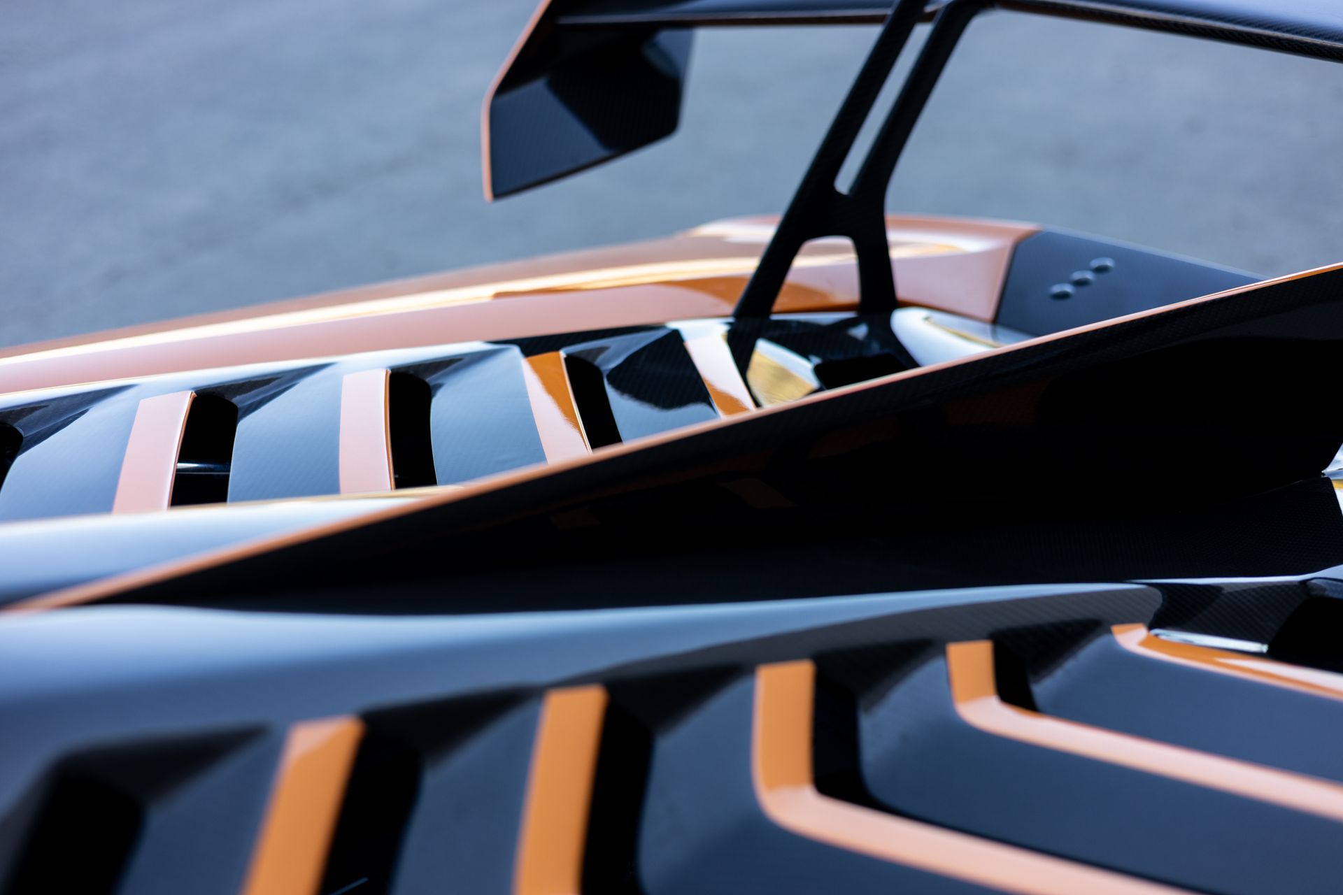 Black and copper sports car with a prominent rear wing. Close-up view of the rear deck and vents.