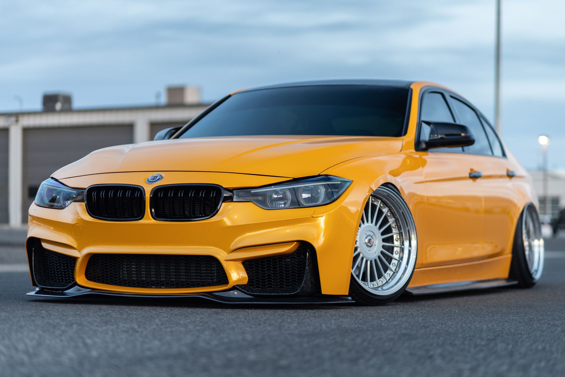 Yellow BMW sedan with black accents, lowered stance, and custom wheels parked on pavement.