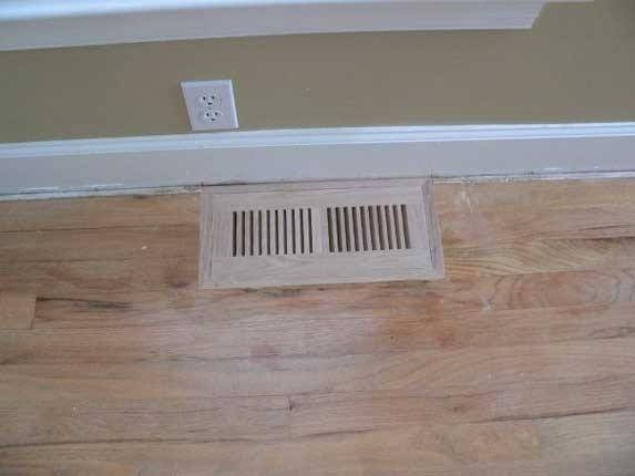 Floor vent on hardwood floor, near wall with electrical outlet.