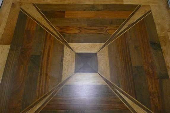 Wooden floor with a geometric, three-dimensional design using various wood tones, creating an optical illusion.