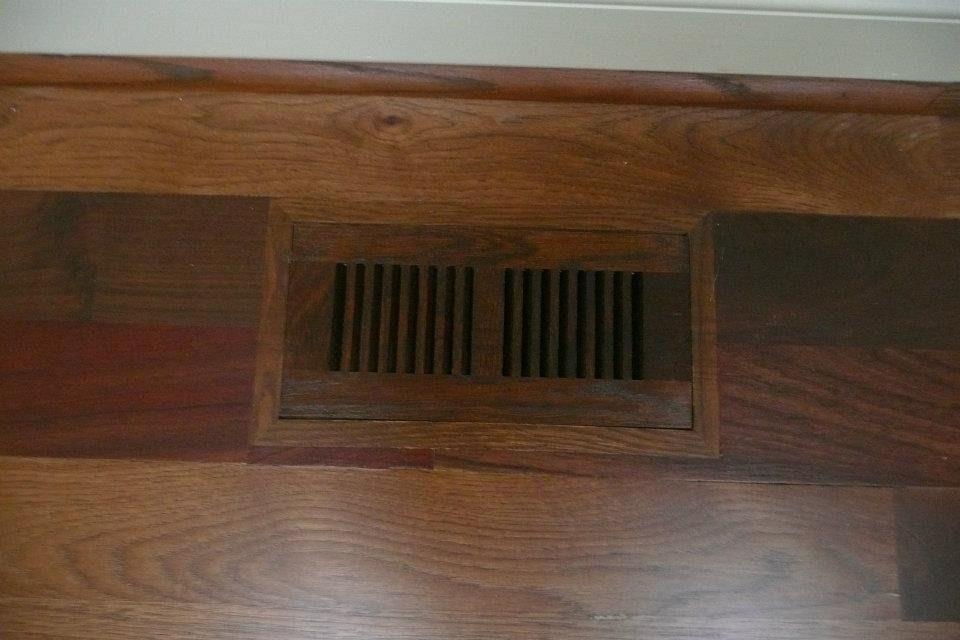 Floor vent with dark wood slats, set in hardwood flooring.