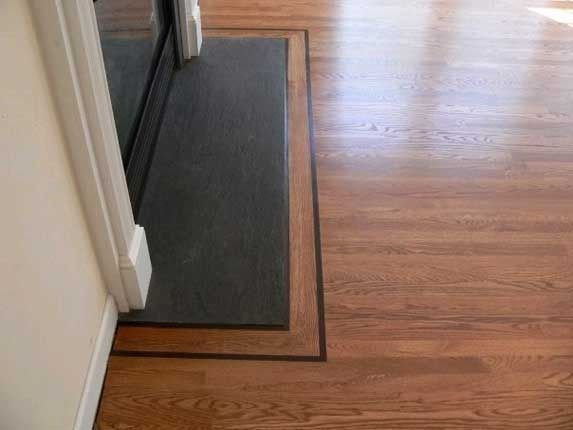 Hardwood floor with dark border around a black mat by a fireplace.