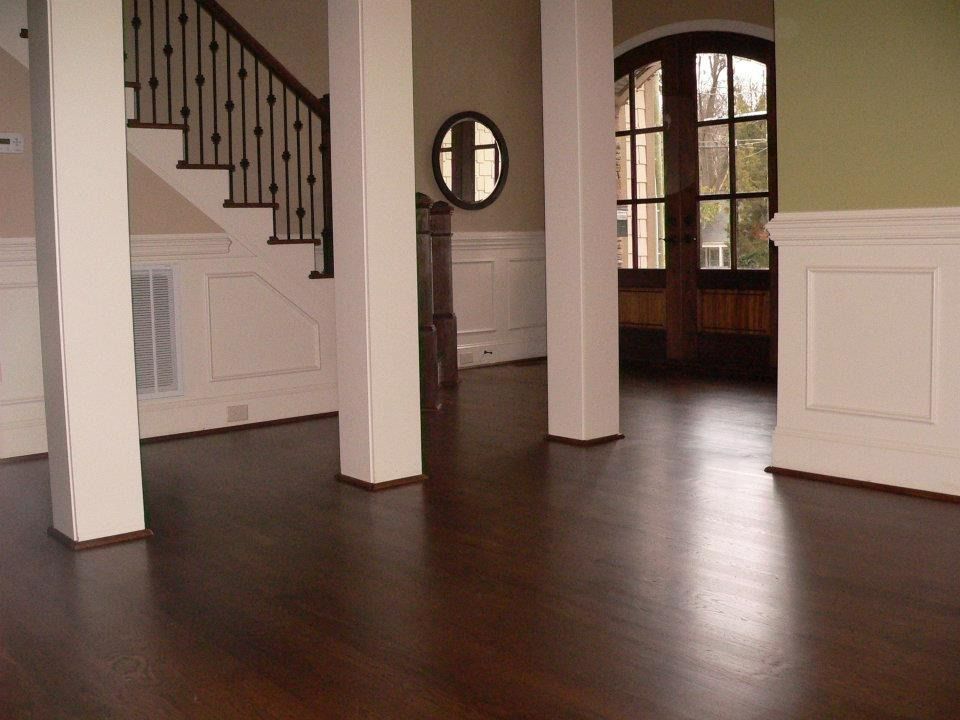 Hardwood floor interior with white columns, stairs, and wainscoting. Dark wood door and a round mirror are visible.