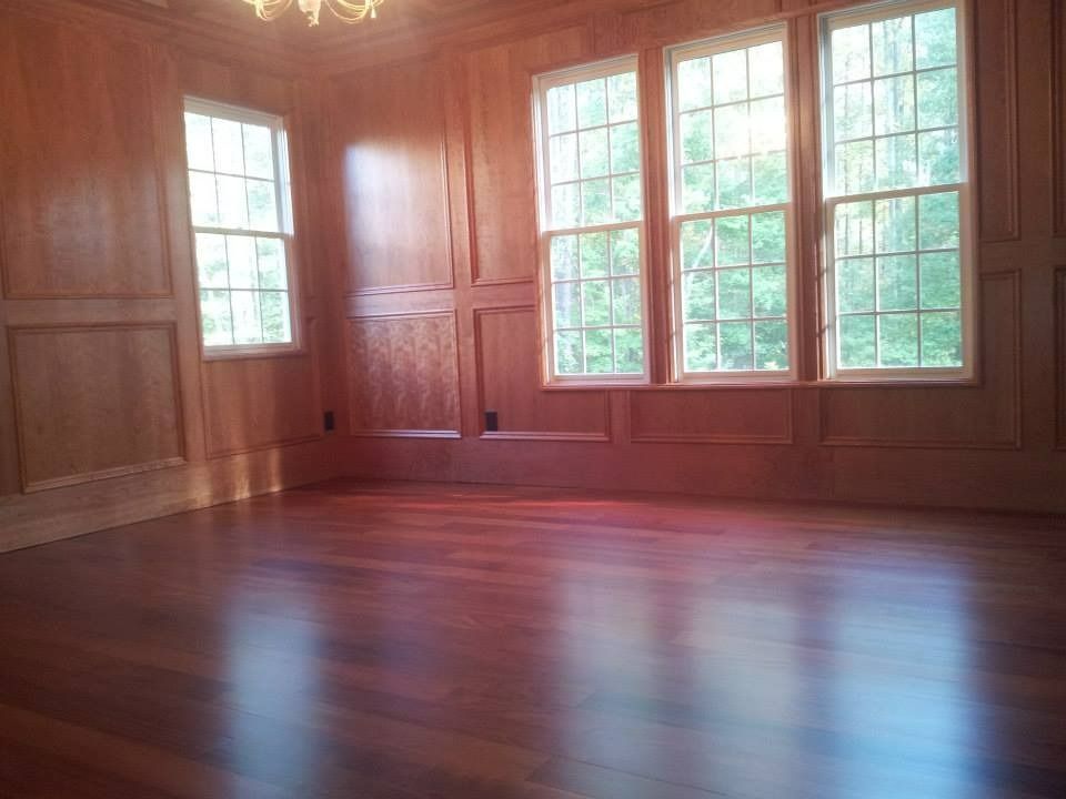 Empty room with wood paneling, windows, and polished hardwood floor.