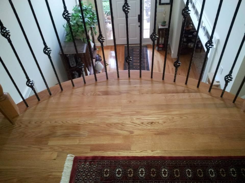 Wooden curved staircase leading to a doorway with a rug. Black iron balusters with decorative scrollwork.