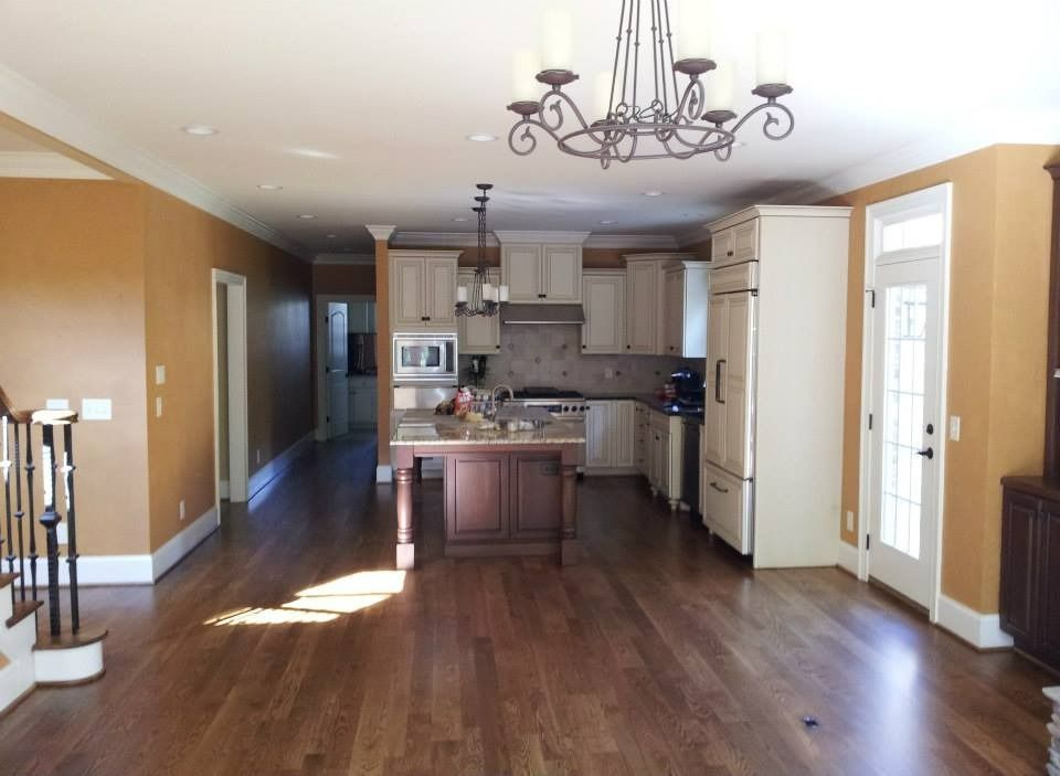 Open-plan kitchen and living area with brown floors, white cabinets, and gold walls.