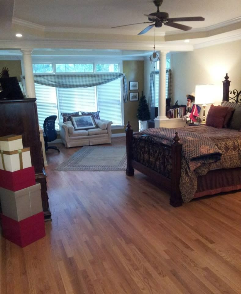 Spacious bedroom with hardwood floors, a bed, sofa, and desk area. A stack of gift boxes sit in front of a dark cabinet.