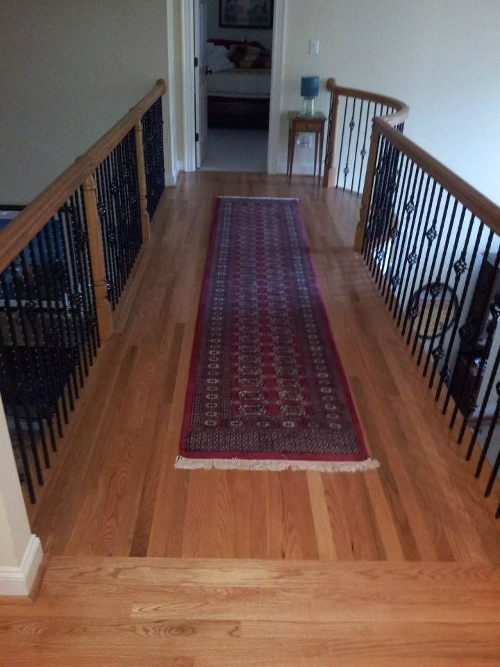 Hallway with hardwood floors, rug, stairs, and ornate black railing with wooden handrail.
