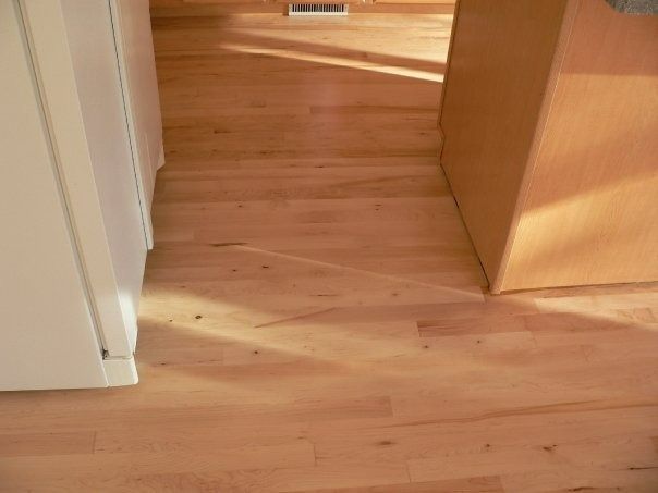 Light wood flooring in a kitchen, seen between a white cabinet and a wooden counter base.