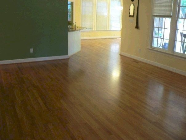 Hardwood floors in a living room with green and beige walls. Sunlight reflects off the floor.