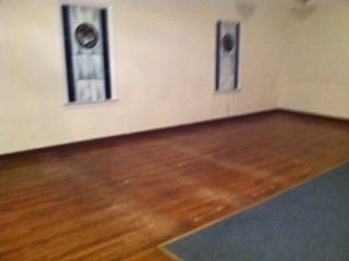 Empty room with hardwood floor, blue carpet edge, cream walls, and decorative wall hangings.