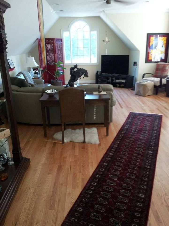 Living room with hardwood floors, sofa, red rug, and a tall, arched window.