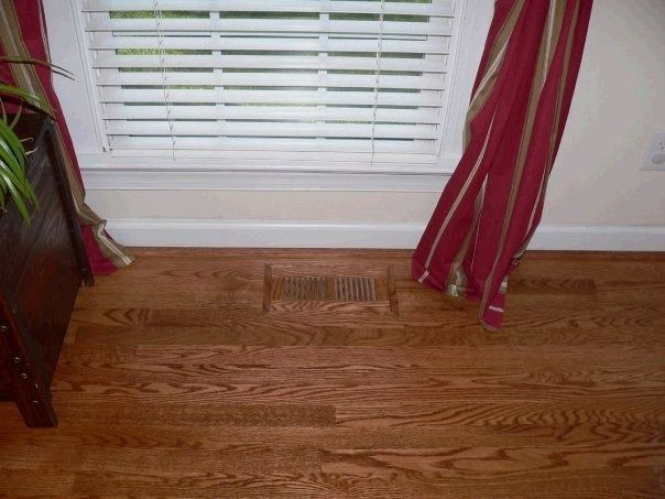 Hardwood floor with a vent, window with blinds, and burgundy curtains.