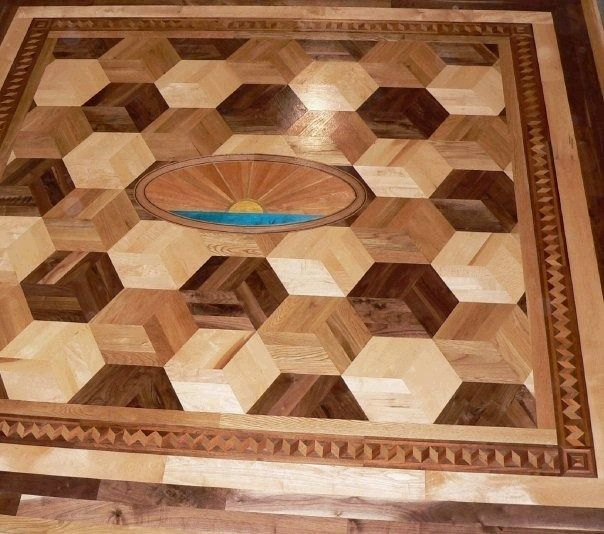 Wooden floor with a 3D cube pattern and a central oval depicting a sunrise over water, surrounded by a decorative border.