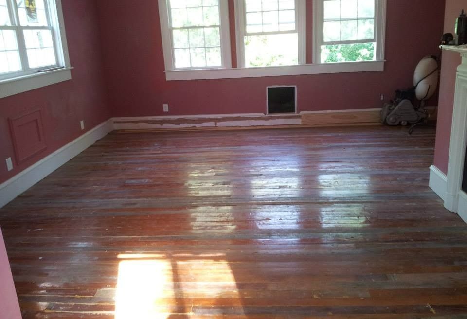 Room with worn wooden floors, burgundy walls, white trim, and three windows.