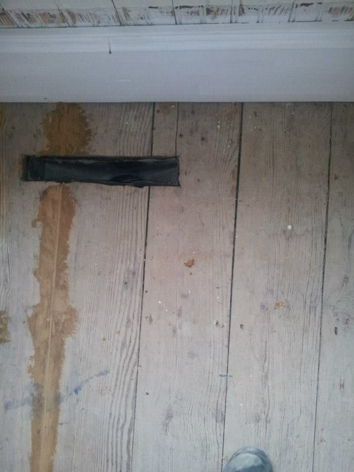 Wooden floorboards with dark tape covering a gap, beneath a white ceiling trim.